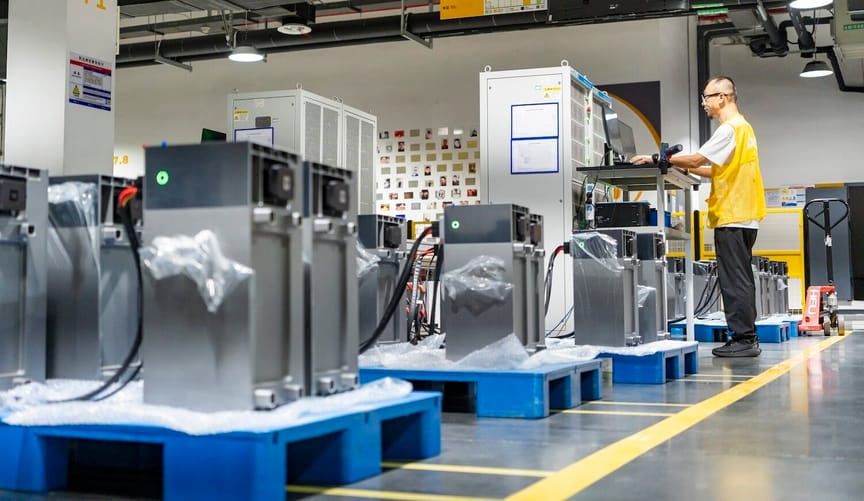 Factory scene with worker in yellow vest and silver battery products on blue platforms
