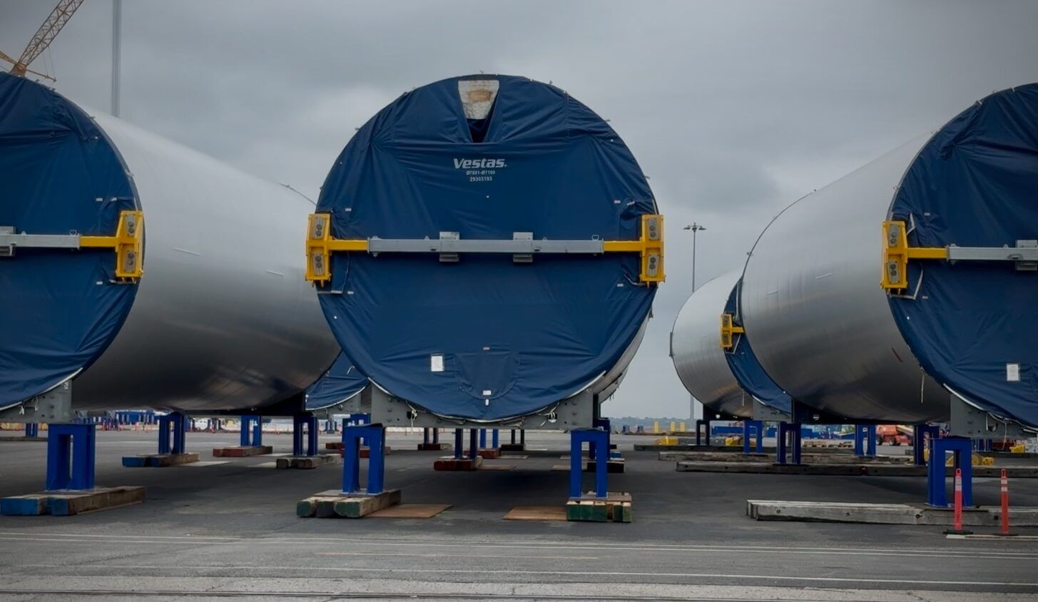 White wind turbine parts on a concrete lot; blue material covering the end