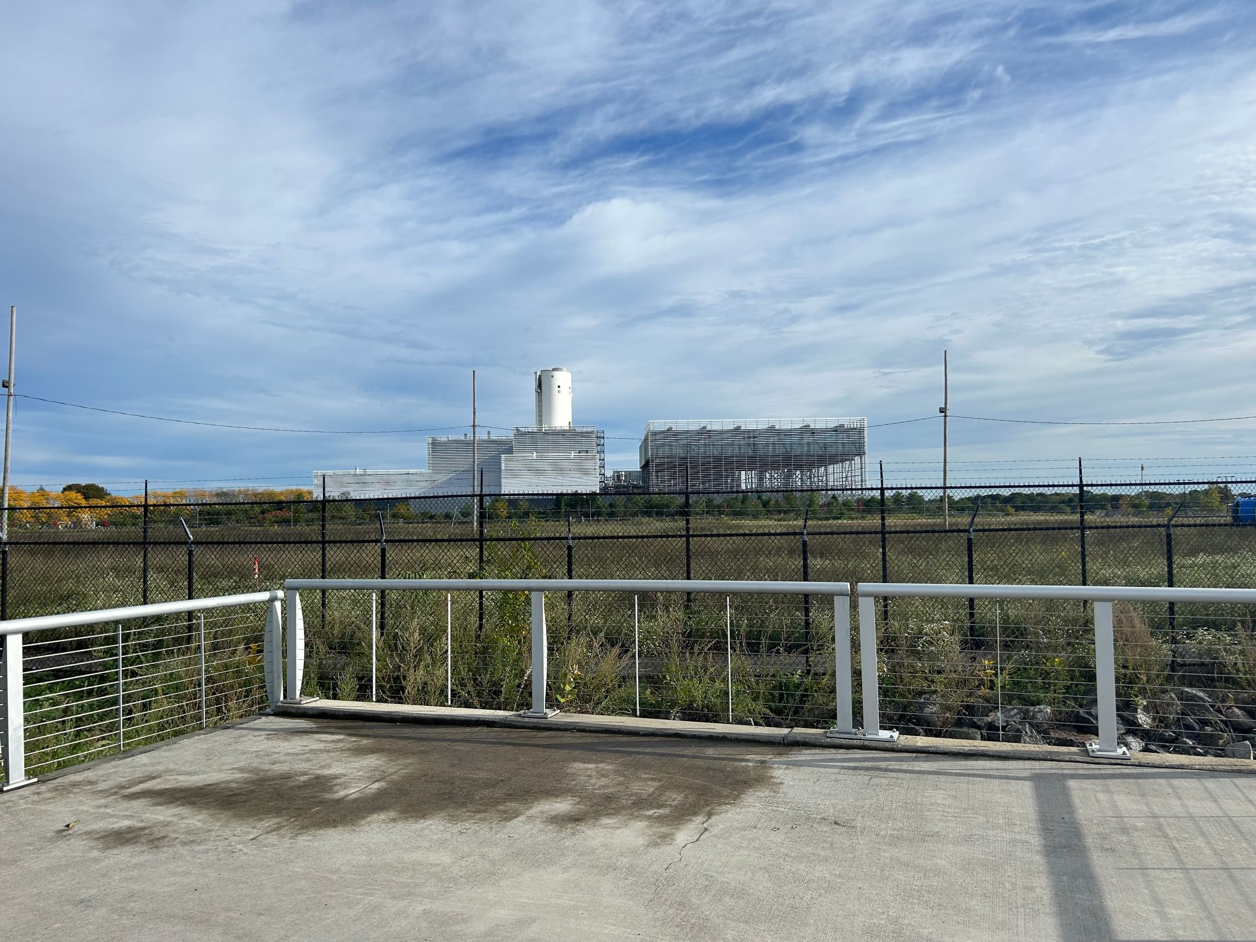 gas plant in the distance, grassy field before it, backdrop of blue sky