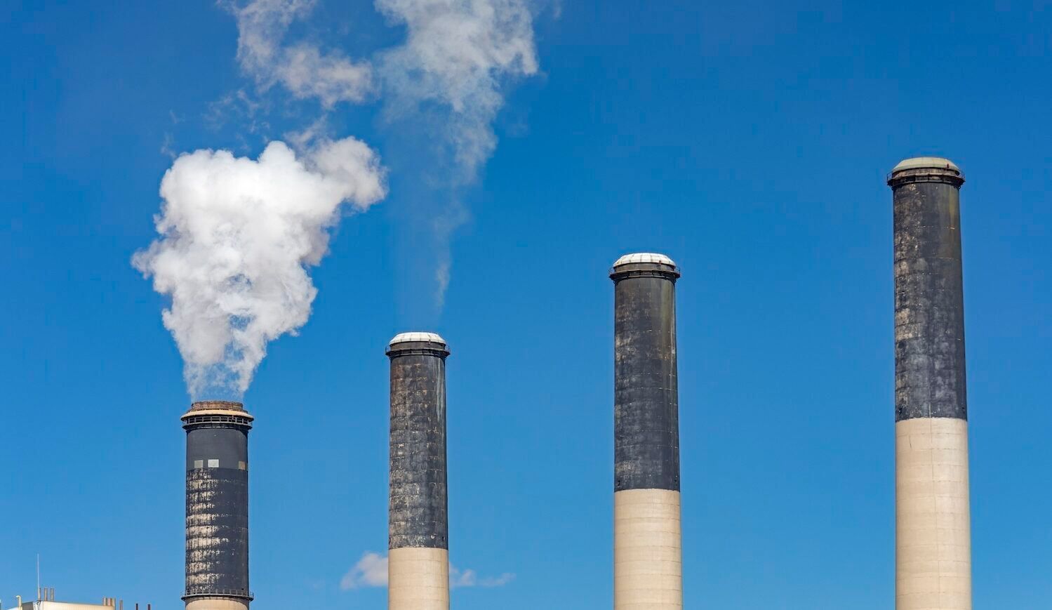 Four smokestacks, light with black tips, two emitting smoke; background is a blue sky