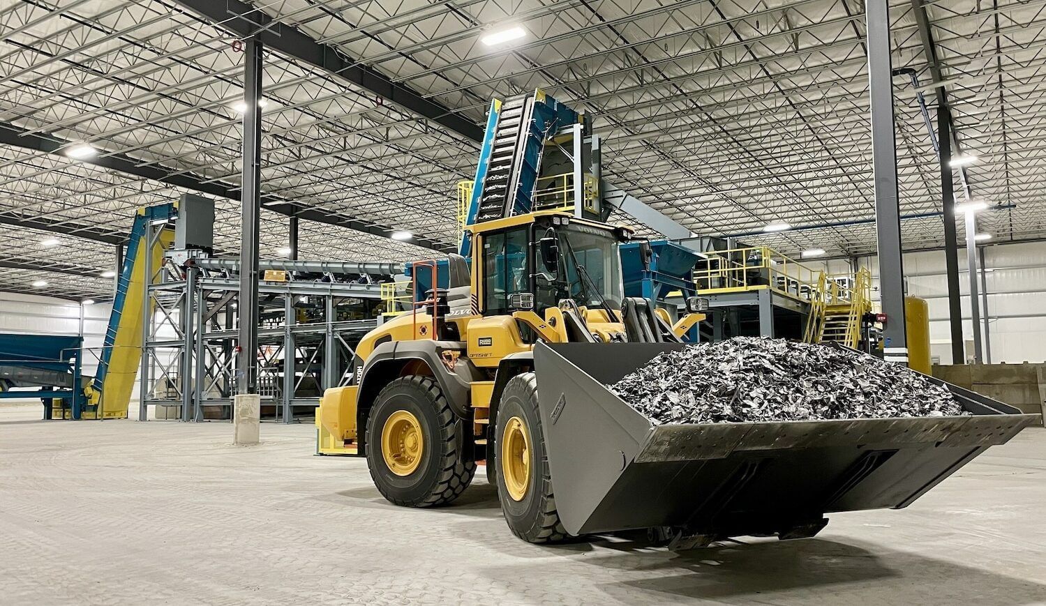 A backhoe loader filled with metal shavings inside a tidy warehouse building with a concrete floor