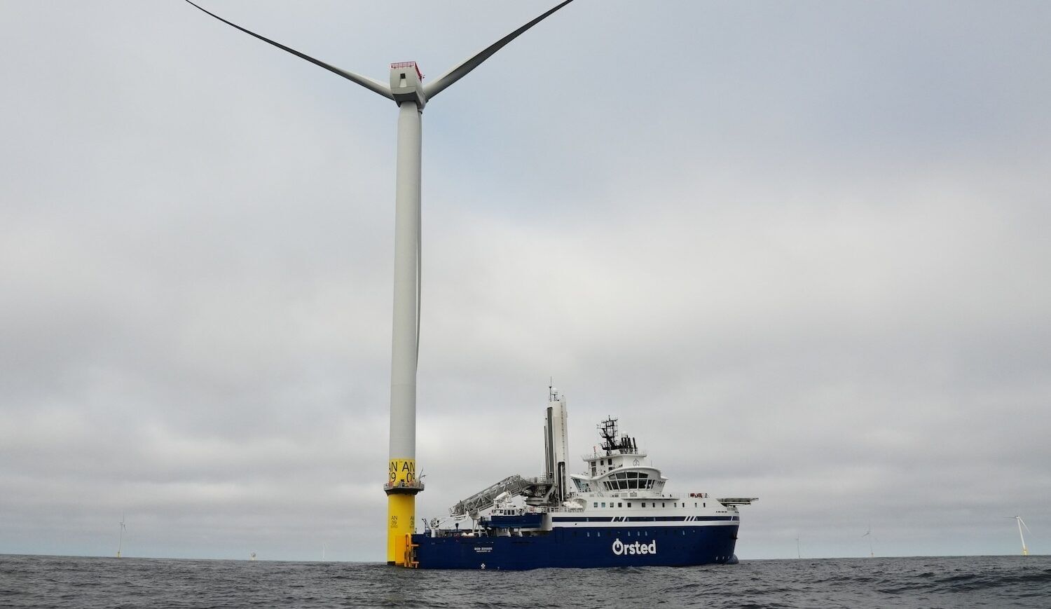 Offshore wnd turbine with a yellow base with an Ørsted boat nearby