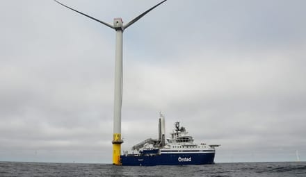 Offshore wnd turbine with a yellow base with an Ørsted boat nearby
