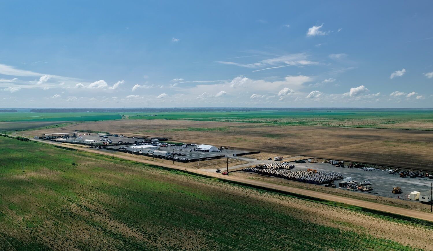 Overhead view of a remote construction site with steel coils, tents, and cars on sunny day with a few clouds in the distance