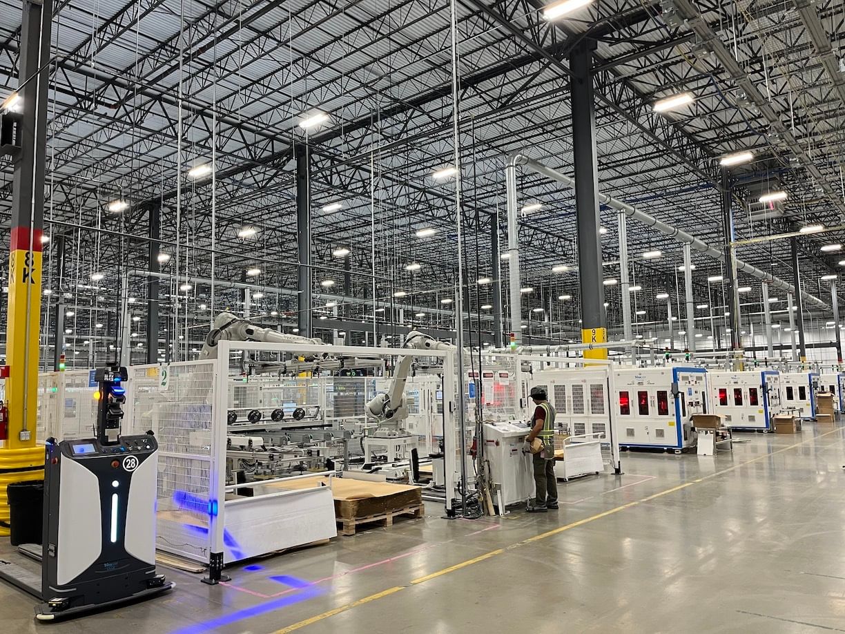 A worker in a large, clean fabrication fabrication facility filled with equipment on a shiny gray floor