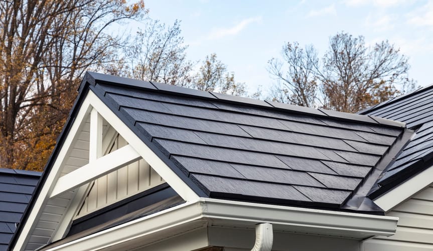 Close-up of roof with solar panels that look like black roof tiles, brick and white wood home