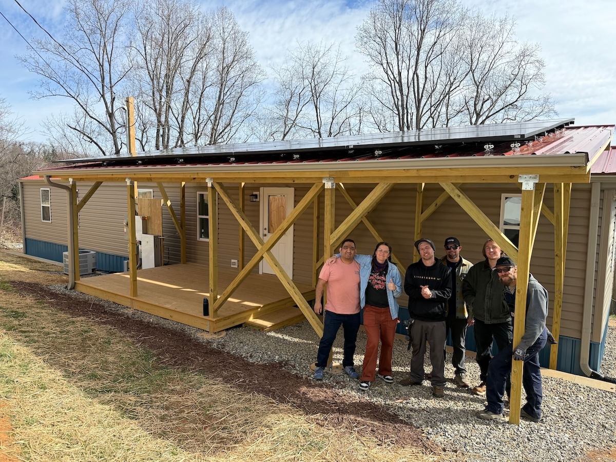 Six people standing in the shade of a newly-constructed solar front porch attached to a mobile home near Asheville, NC