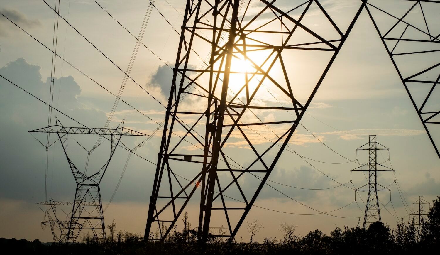 Transmission towers with the sun shining through clouds in the background