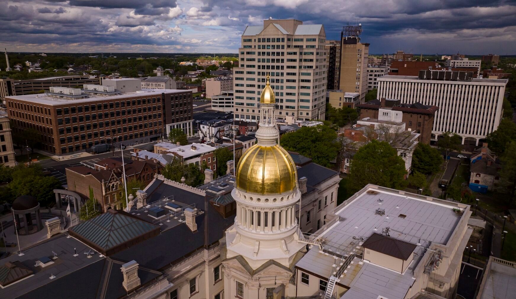 Gold-domed statehouse surrounded by buildings of various heights, under a cloudy sky