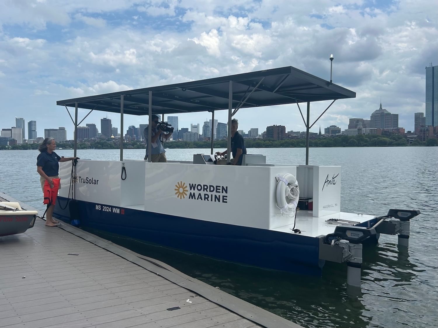 Blue-and-white boat with "Worden Marine" at a doc with city skyline in background; two people on boat, one on dock