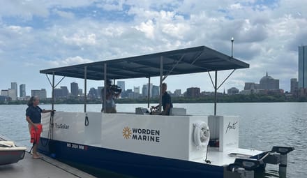 Blue-and-white boat with "Worden Marine" at a doc with city skyline in background; two people on boat, one on dock