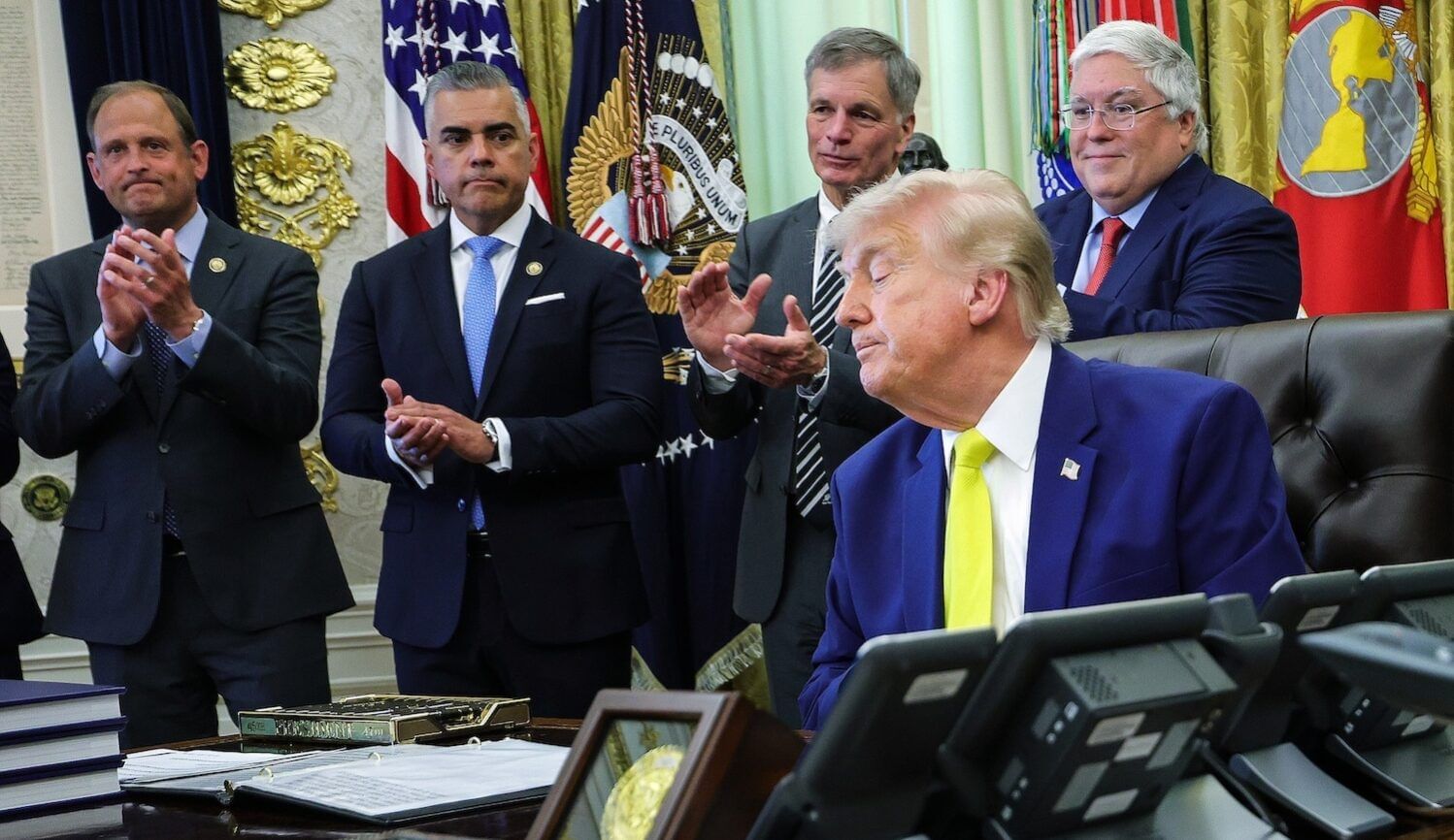 Trump at a desk with four men applauding behind him
