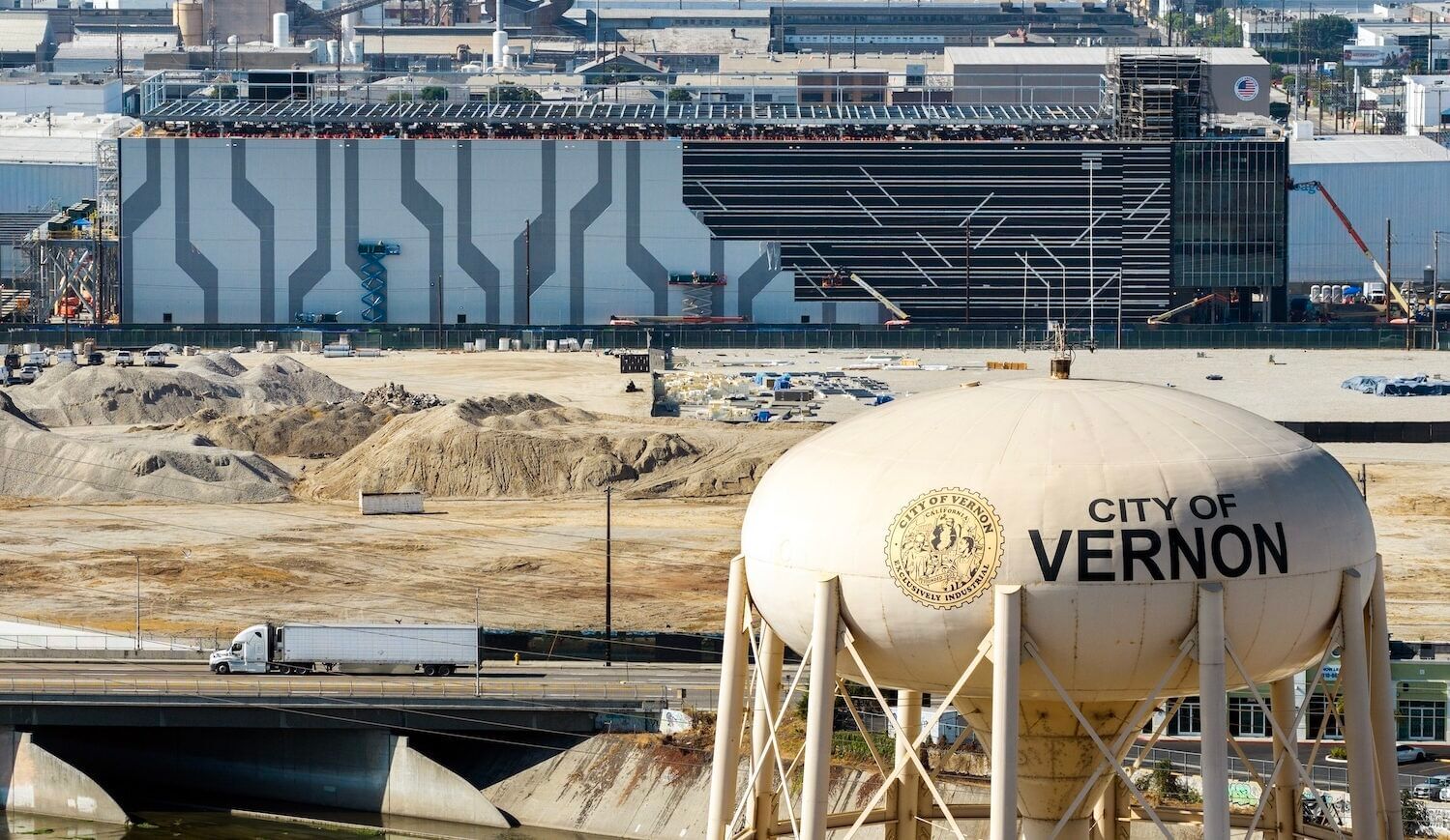 Mid-rise data center being built on a dirt lot with "City of Vernon" water tower in foreground