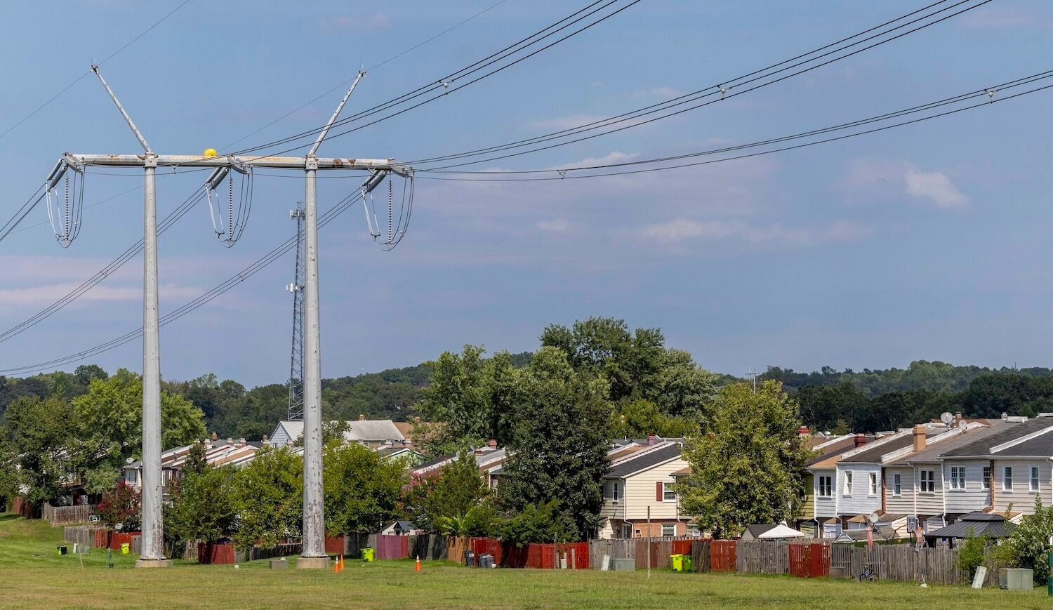 Power line on a grassy strip with a suburban housing development running alongside on the right