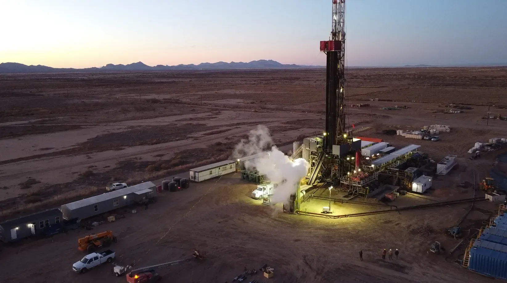 Geothermal well site at at dusk or sunrise, with a lights shining on worksite