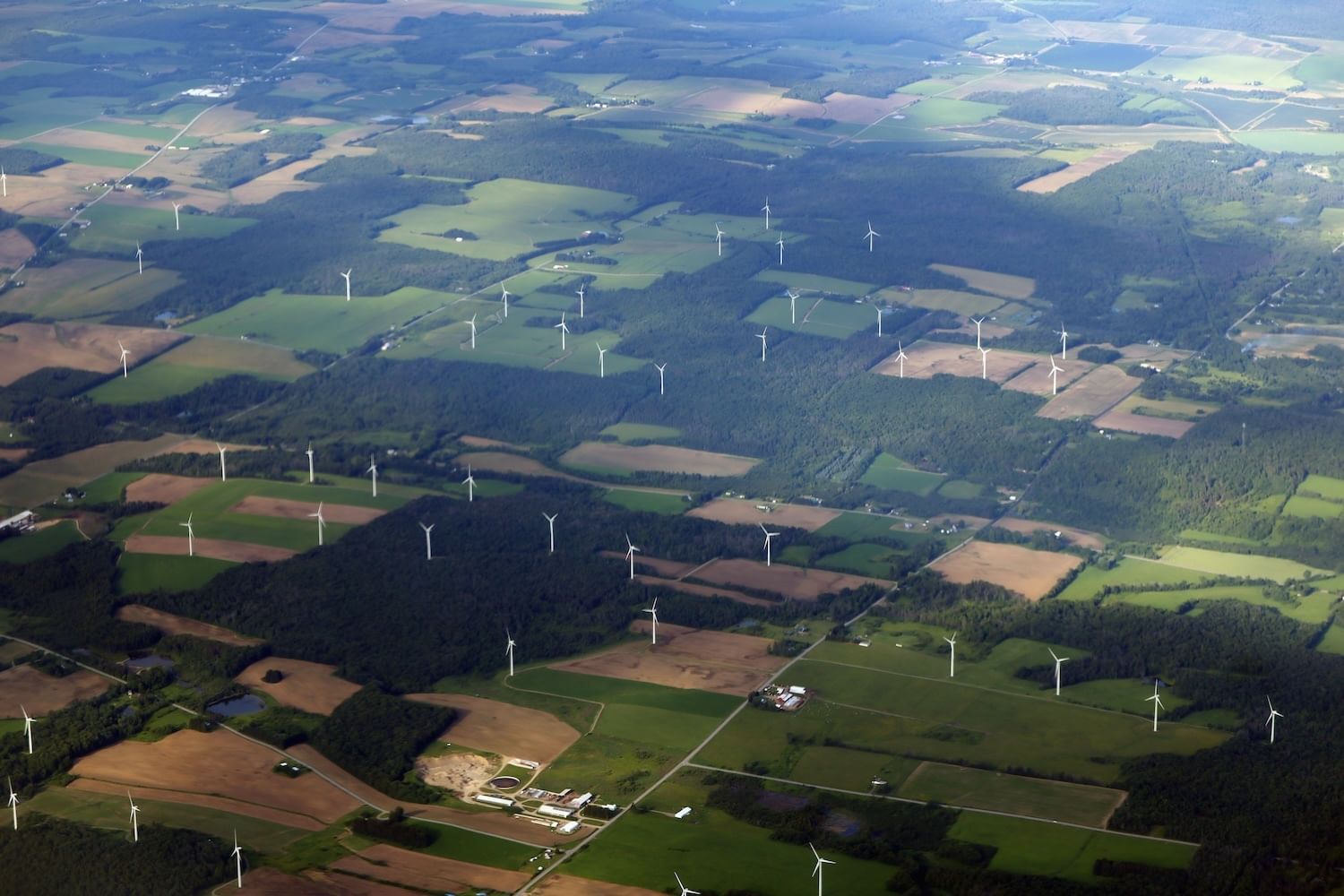 Aerial shot of wind turbines on a landscape of grassy, forested, and dirt plots