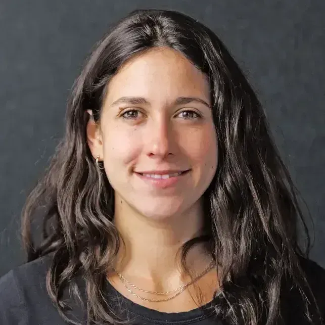 A woman with long brown hair parted in the middle wearing a brown shirt and necklace