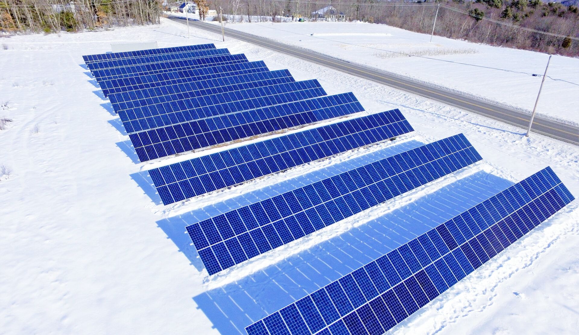 About a dozen rows of solar panels on a snowy lot near a road