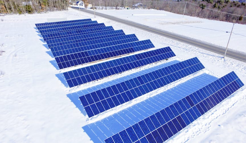About a dozen rows of solar panels on a snowy lot near a road