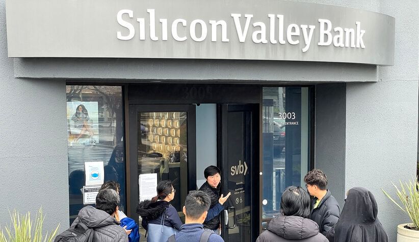 A man stands in an open business doorway talking to a crowd of people outside under a sign that says Silicon Valley Bank