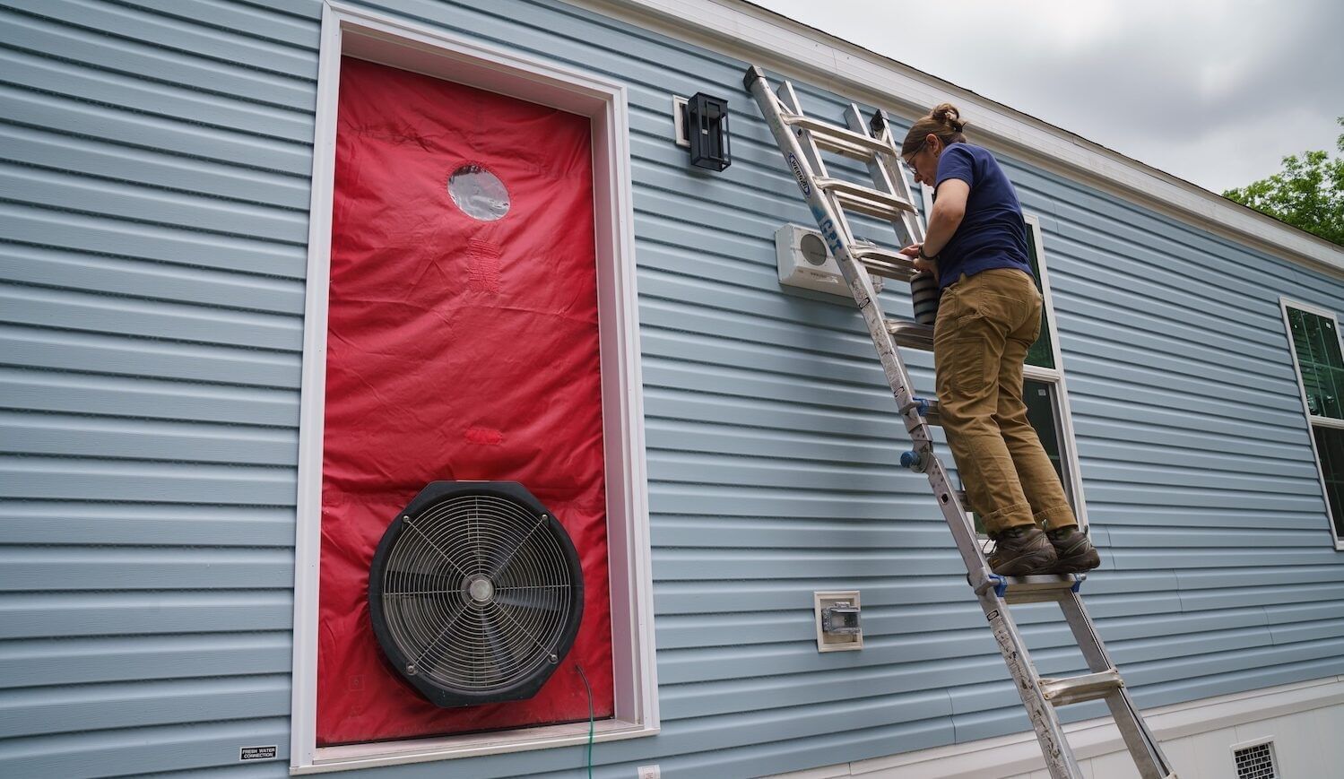 A person on a ladder leaned on a manufactured home.