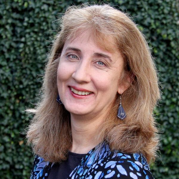 Woman with shoulder-length light brown hair wearing a black top with a blue design
