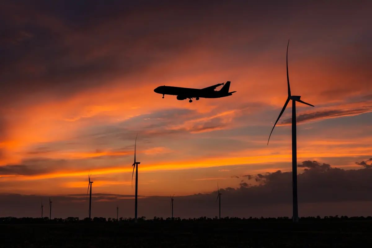 A plane and wind turbines silhouetted at sunset against a cloudy sky