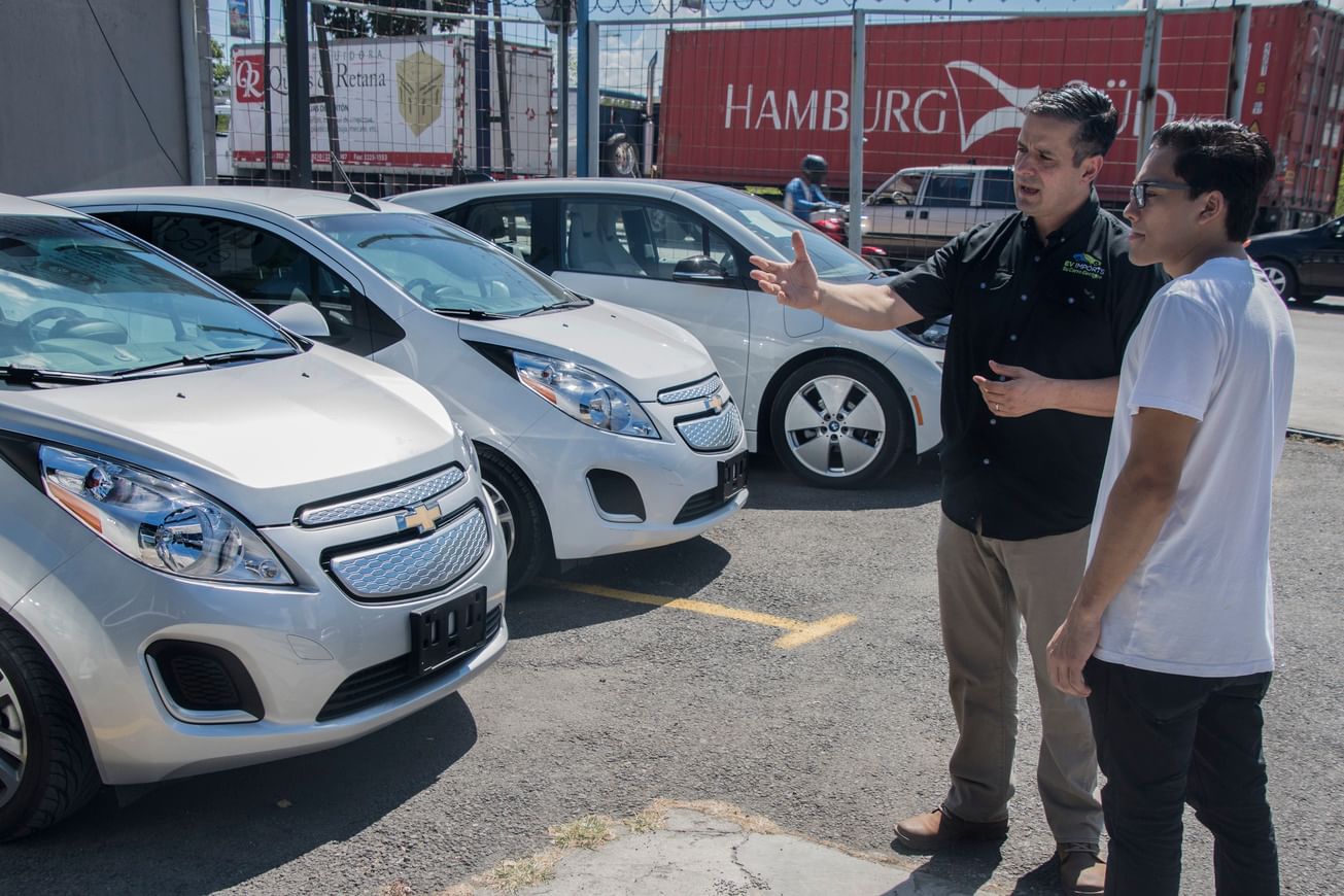 Two men stand in a car dealership lot looking at electric vehicles