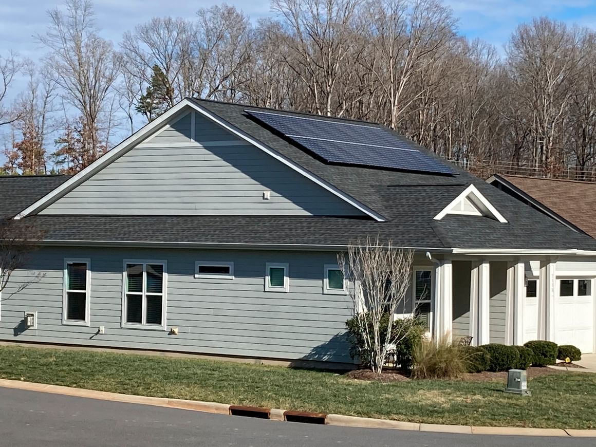 A gray, wood-paneled home with white columns and solar panels on its roof
