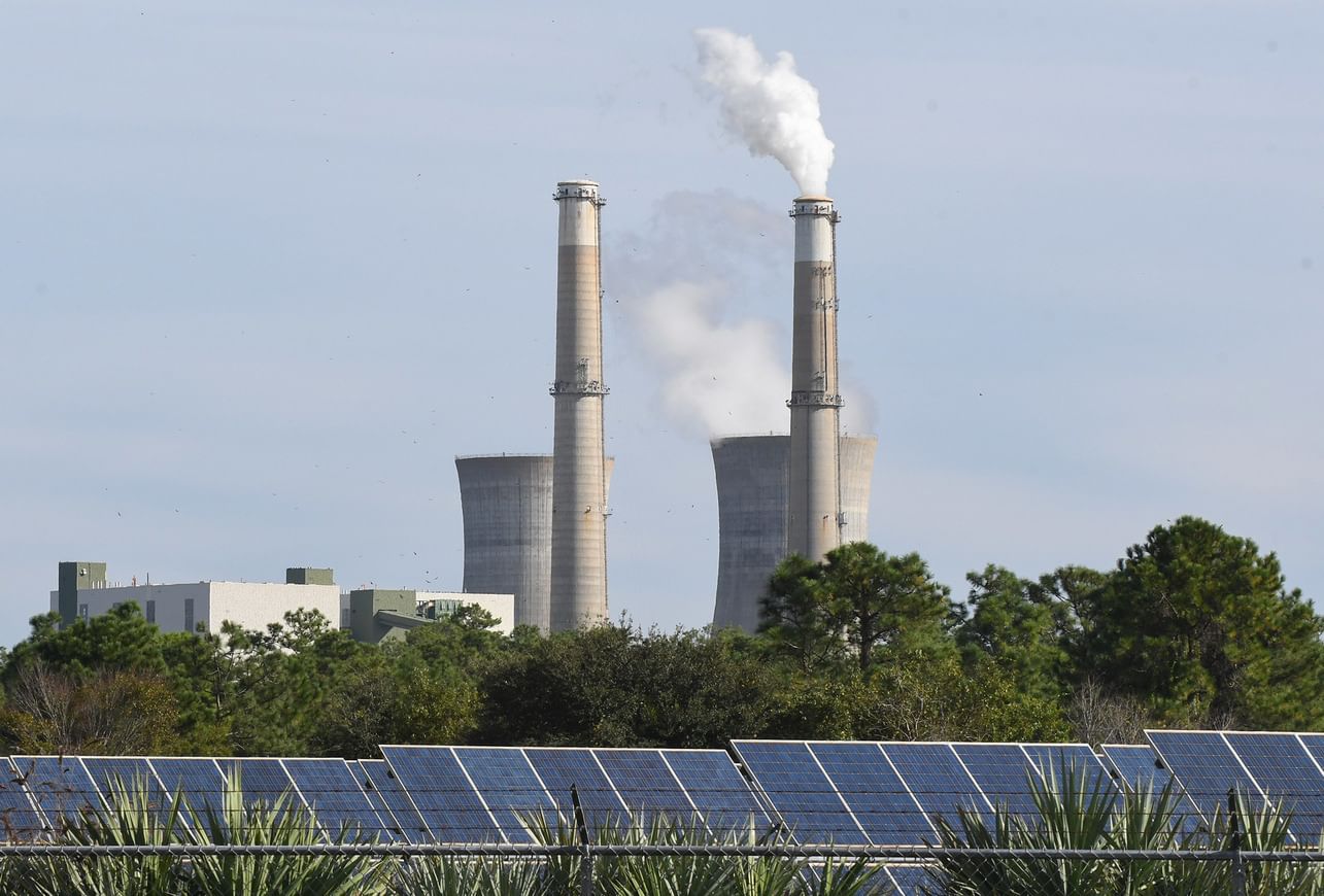 A large solar array in front of the smokestacks of a coal-fired plant