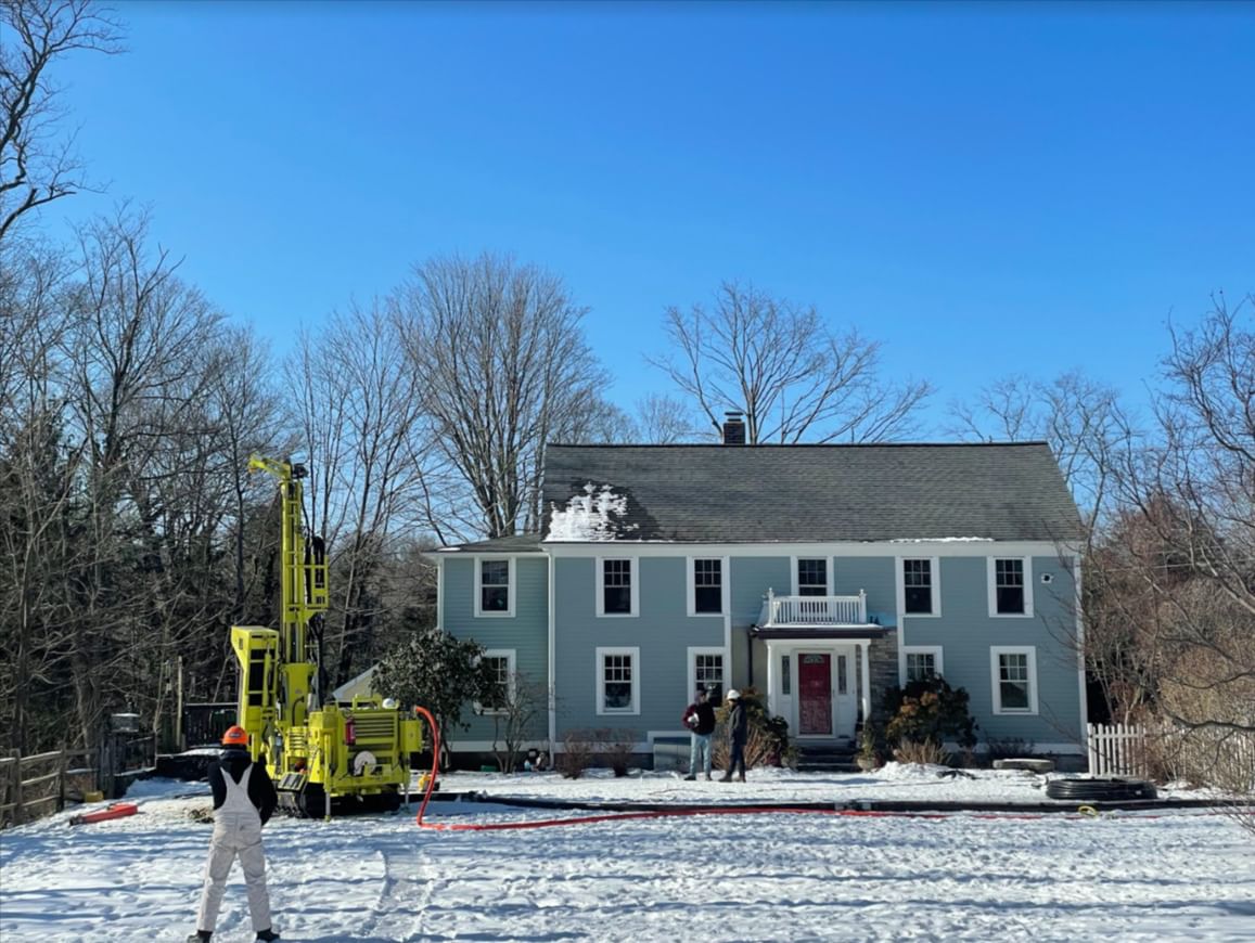 A large drilling rig in front of a two-story blue house