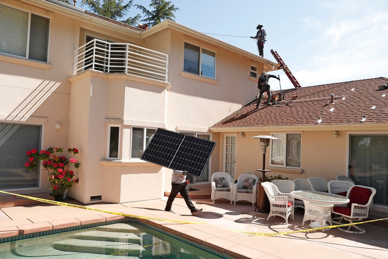 Workers install solar panels on a two-story peach stucco home with a swimming pool