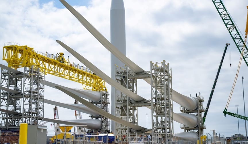 Wind turbines stacked on construction equipment against a cloudy sky