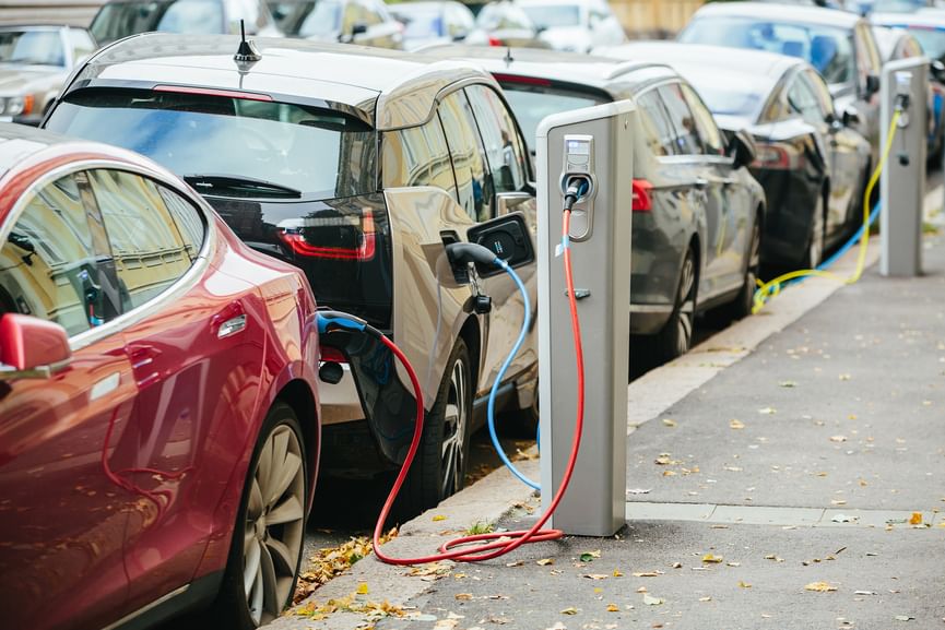 A row of electric vehicles parked on the street and attached to chargers
