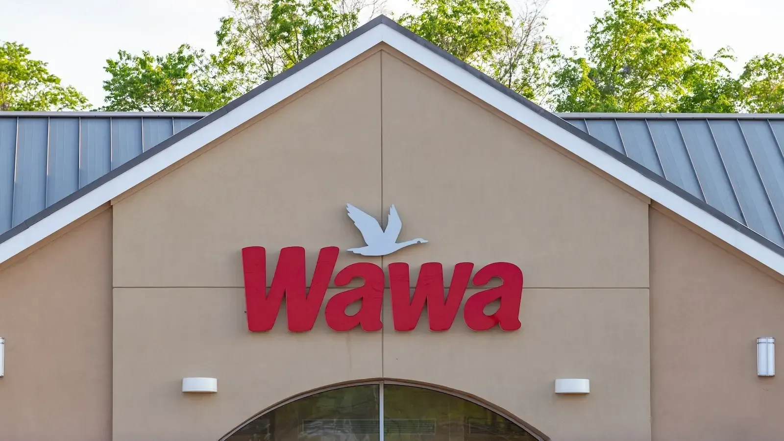 The red convenience-store logo Wawa seen on a tan wall below a gabled roof