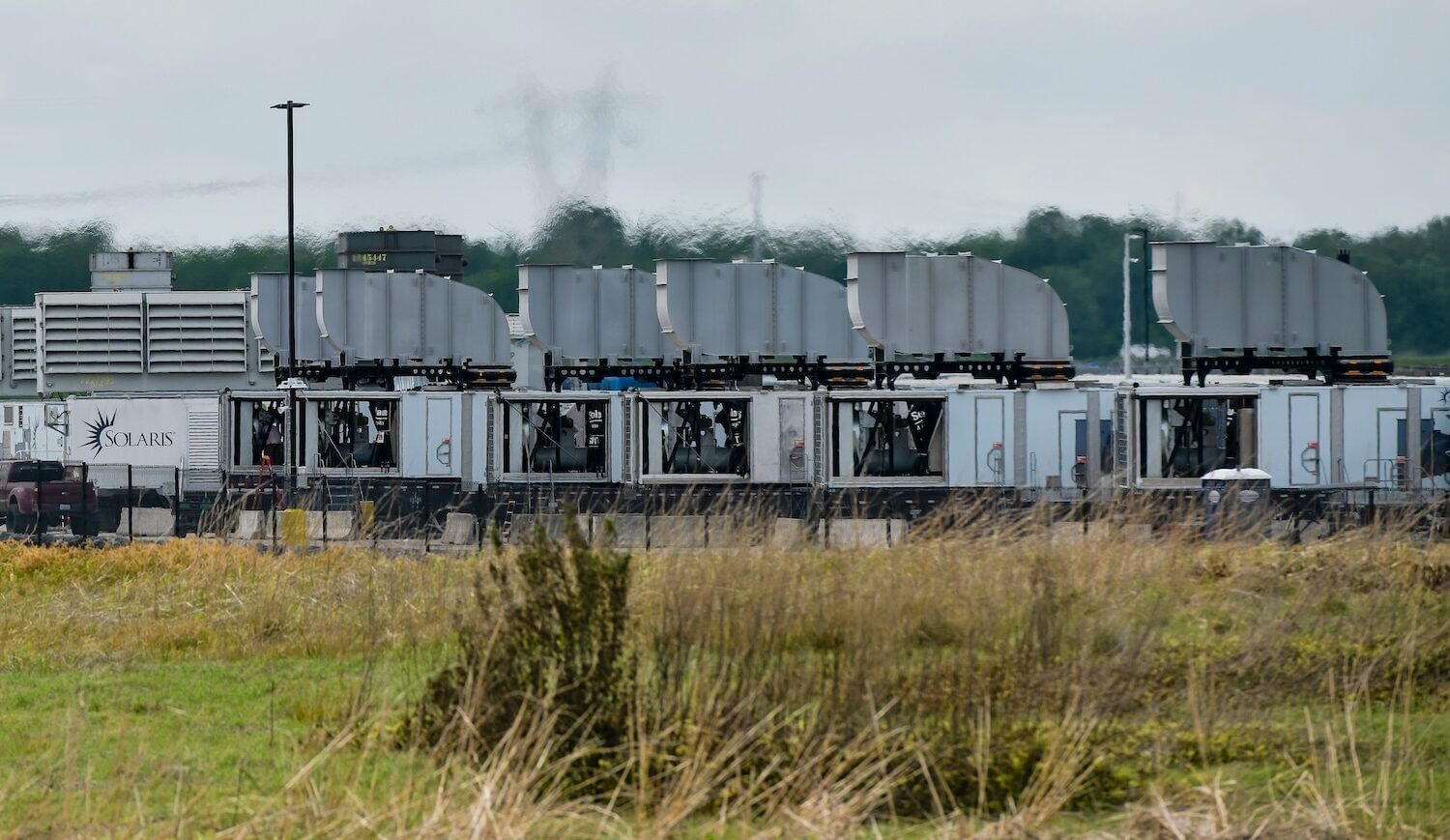 Truck beds with gas generators; grassy lot in foreground